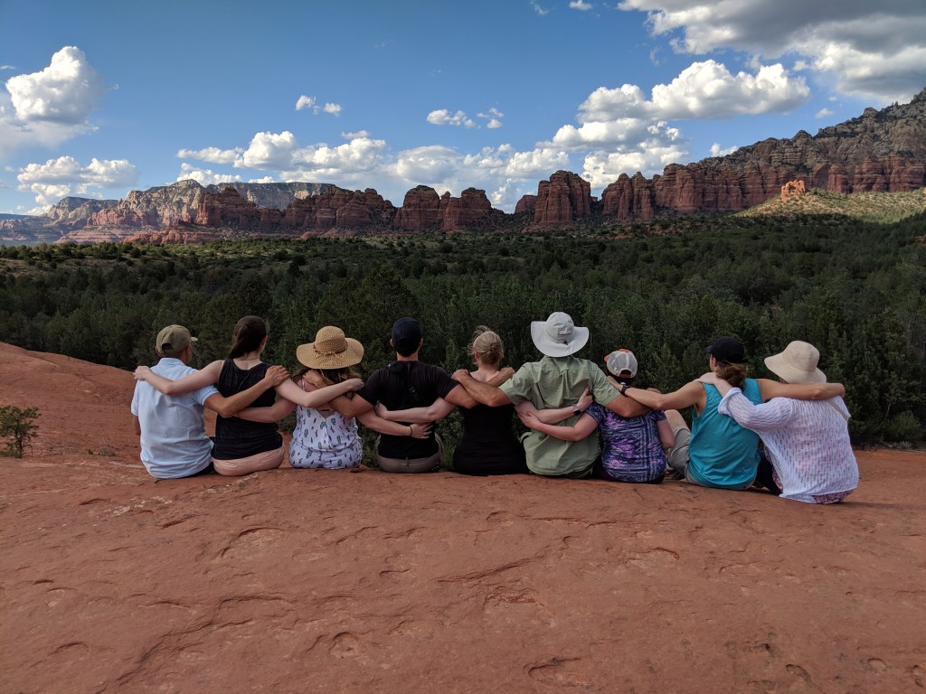 Team VIP sitting down looking out over the red rocks of Sedona. Facing away from the camera with their arms around each other.